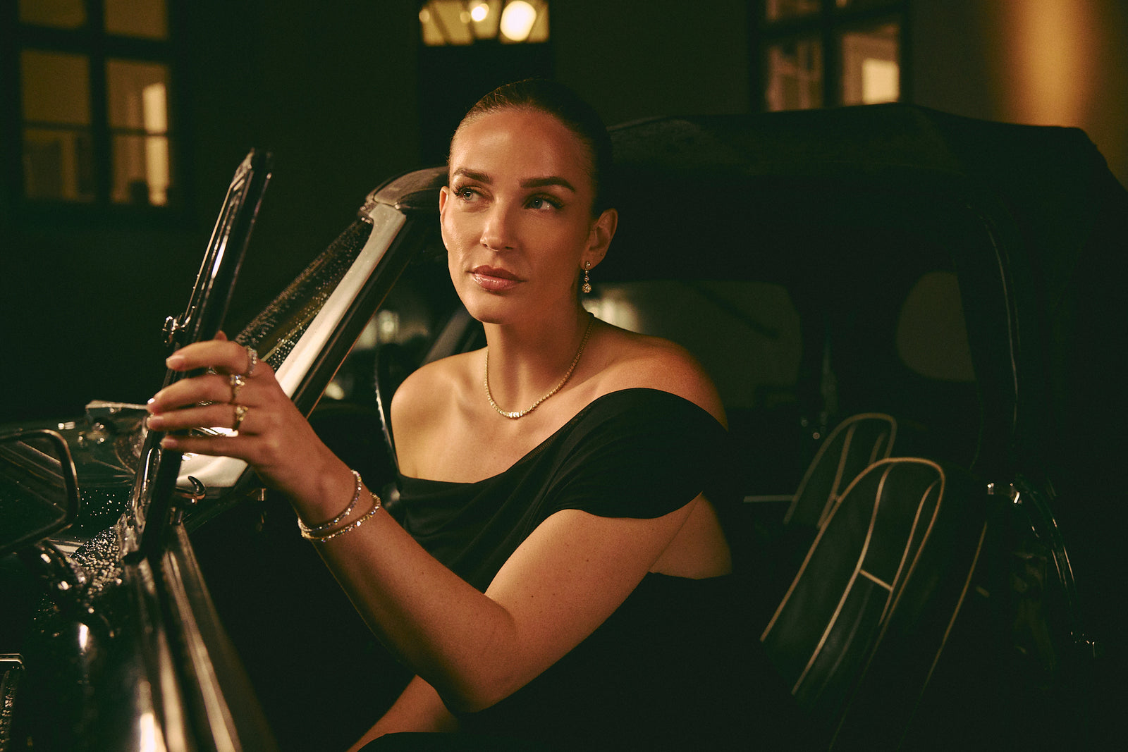 Woman in a black dress wearing lab-grown diamond jewelry in a vintage car